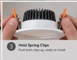 Hands holding both spring clips of a recessed downlight up, ready to install